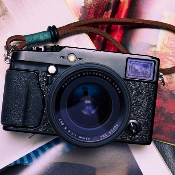 A black Fujifilm camera with a brown strap resting on colorful open magazines.