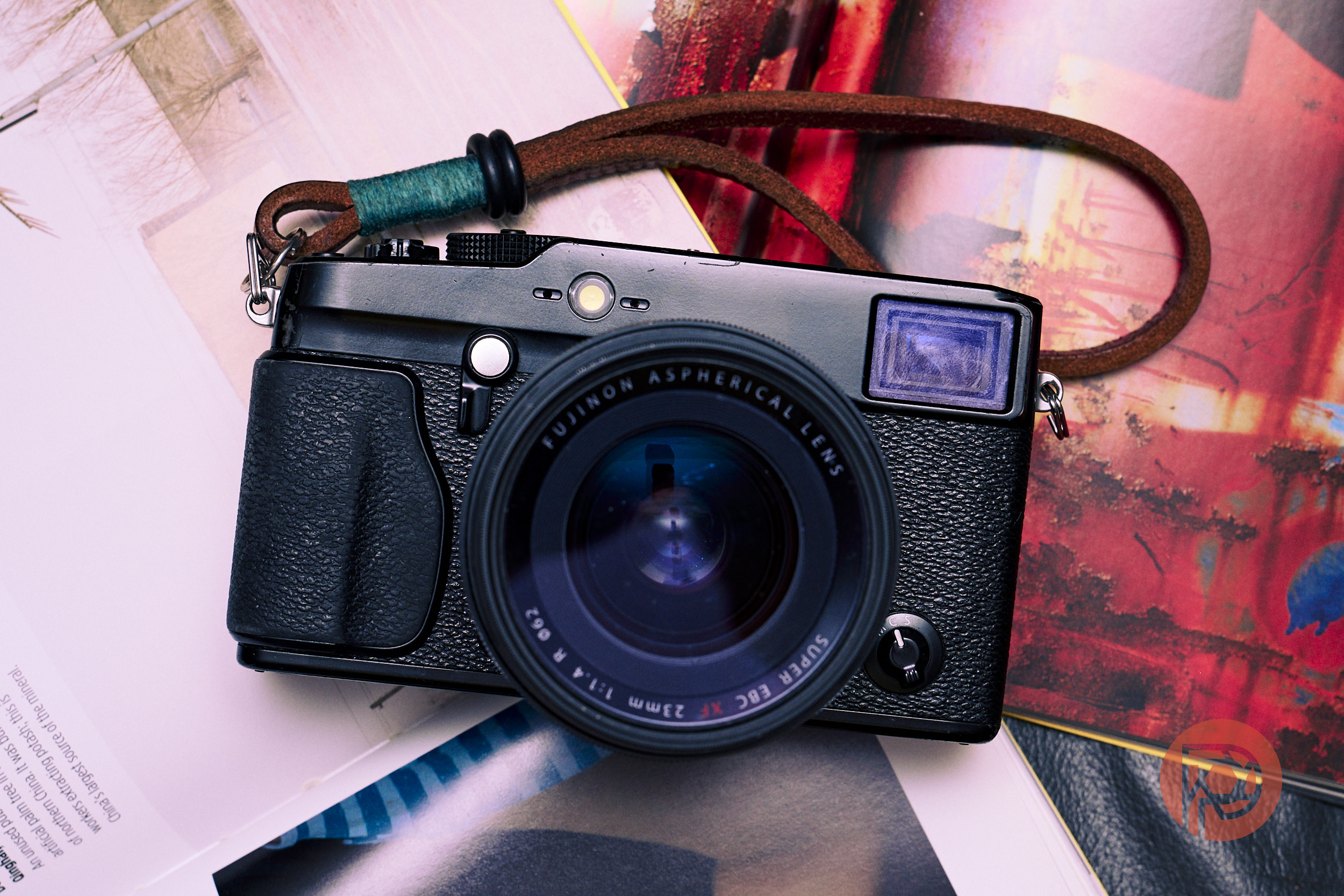 The Camera That Feels Built for Street Photography – The Fujifilm X-Pro in 2026 A black Fujifilm camera with a brown strap resting on colorful open magazines.