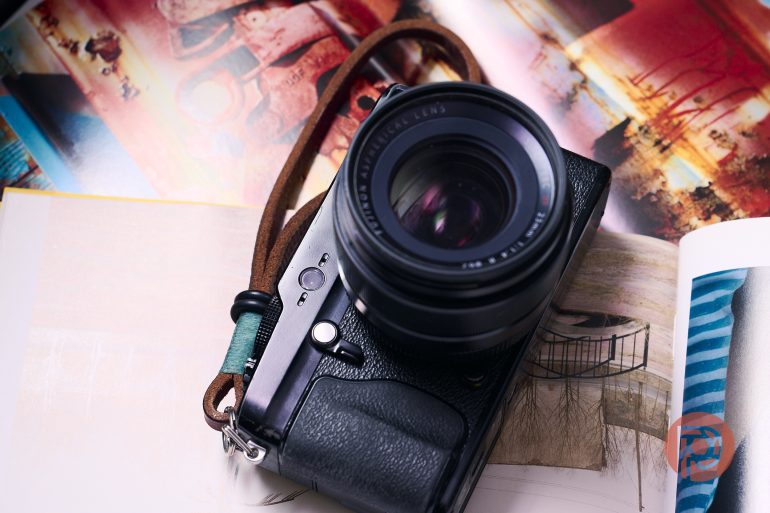 A black camera with a lens and leather strap rests on colorful, open magazines.