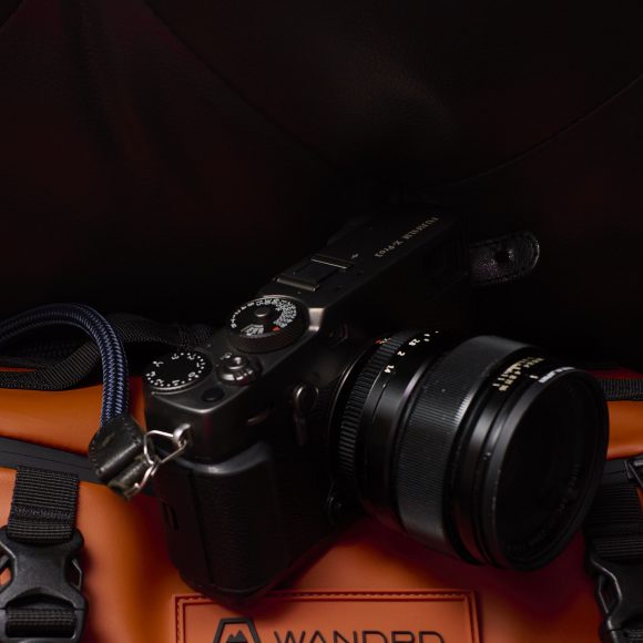A black camera rests on an orange bag with black buckles, set against a dark background.