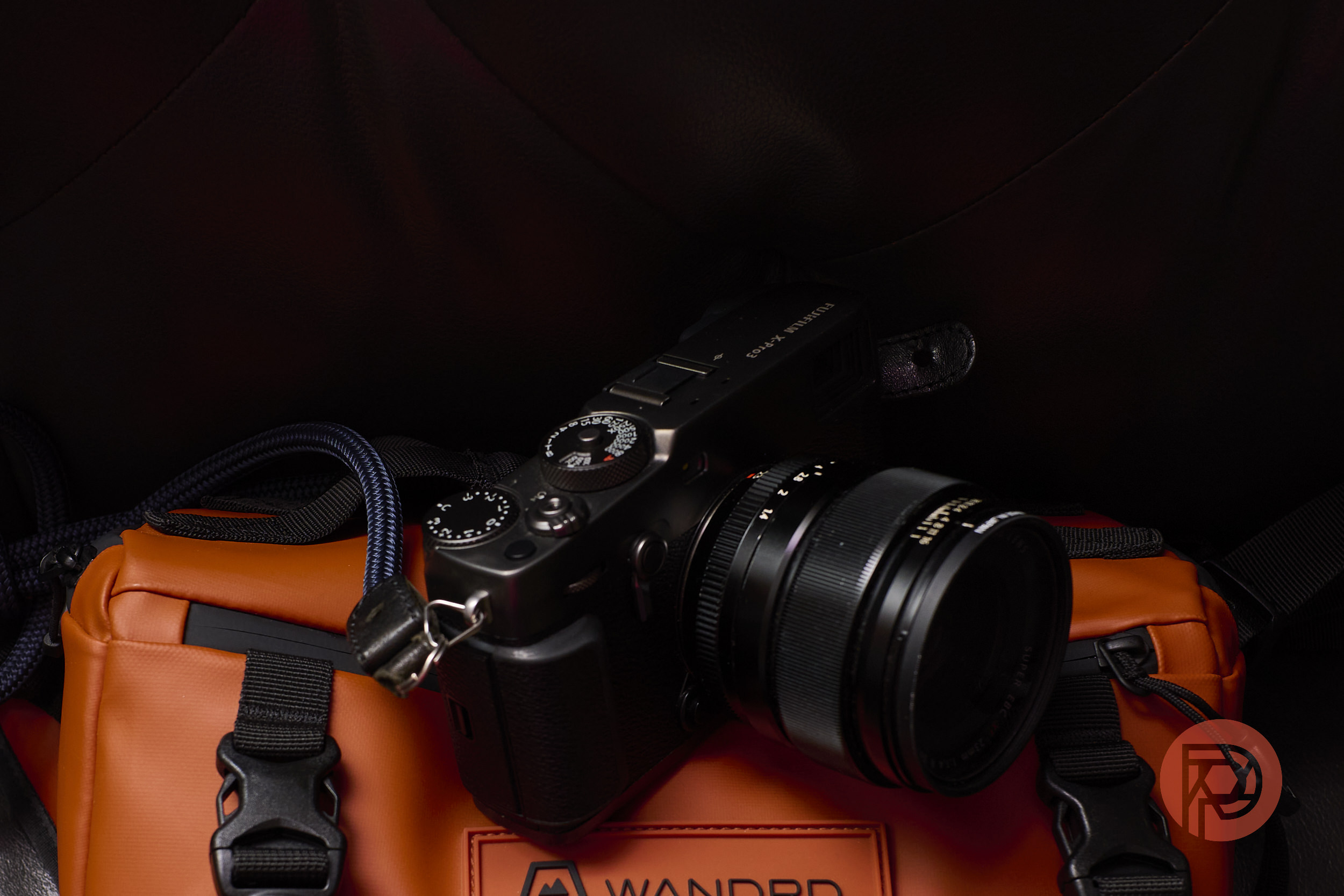 Even in 2026, the X-Pro 3 Still Brings Me Great Joy A black camera rests on an orange bag with black buckles, set against a dark background.