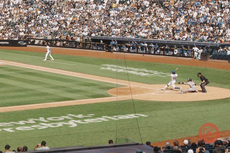 Baseball player swings at a pitch during a game while the crowd watches from the stands.