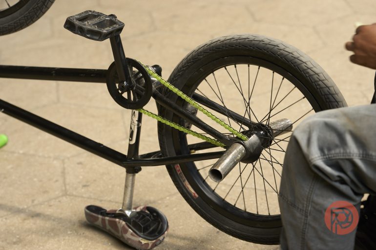 A person sits beside a BMX bike, focusing on the bikes rear wheel and chain.