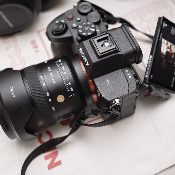 A Sony camera with a large lens and flip-out screen displaying a photo, resting on a white surface.