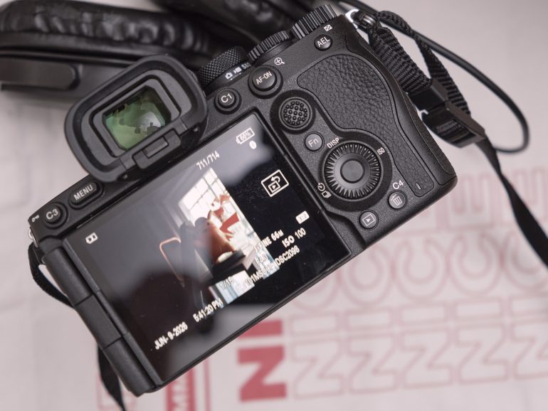 Digital camera showing a photo of a person on its screen, with headphones in the background.