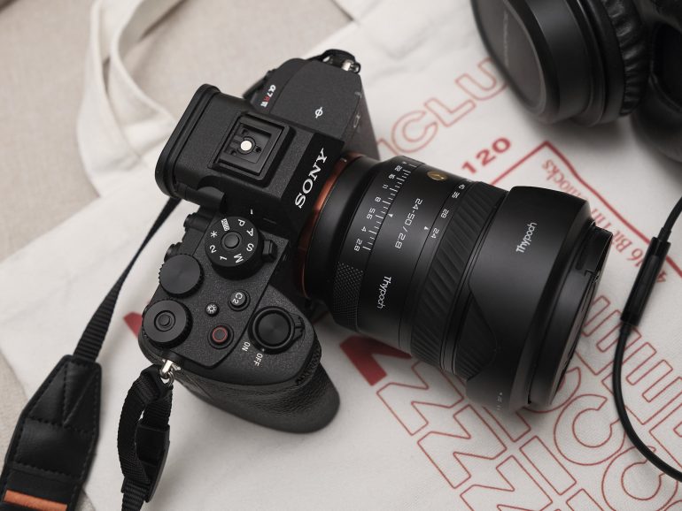 A Sony camera with a Tamron lens sits next to black headphones on a white printed cloth.