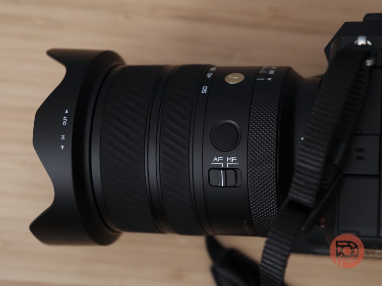 Close-up of a camera lens with AF/MF switch and grip, mounted on a camera body, with a strap visible.