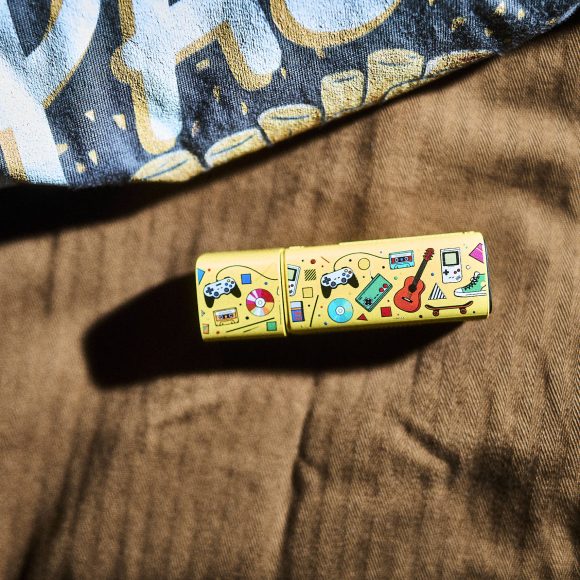 A yellow USB drive with colorful illustrations lies on brown fabric near a patterned shirt.