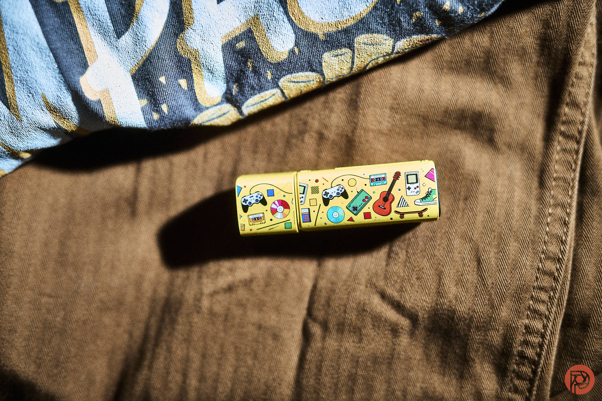 A yellow USB drive with colorful illustrations lies on brown fabric near a patterned shirt.
