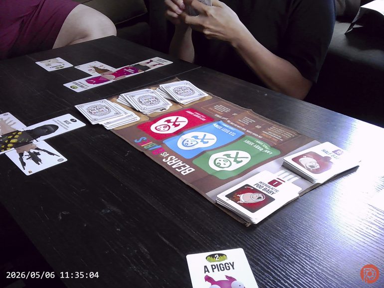 Two people playing a card game called Bears vs Babies at a table with game cards spread out.