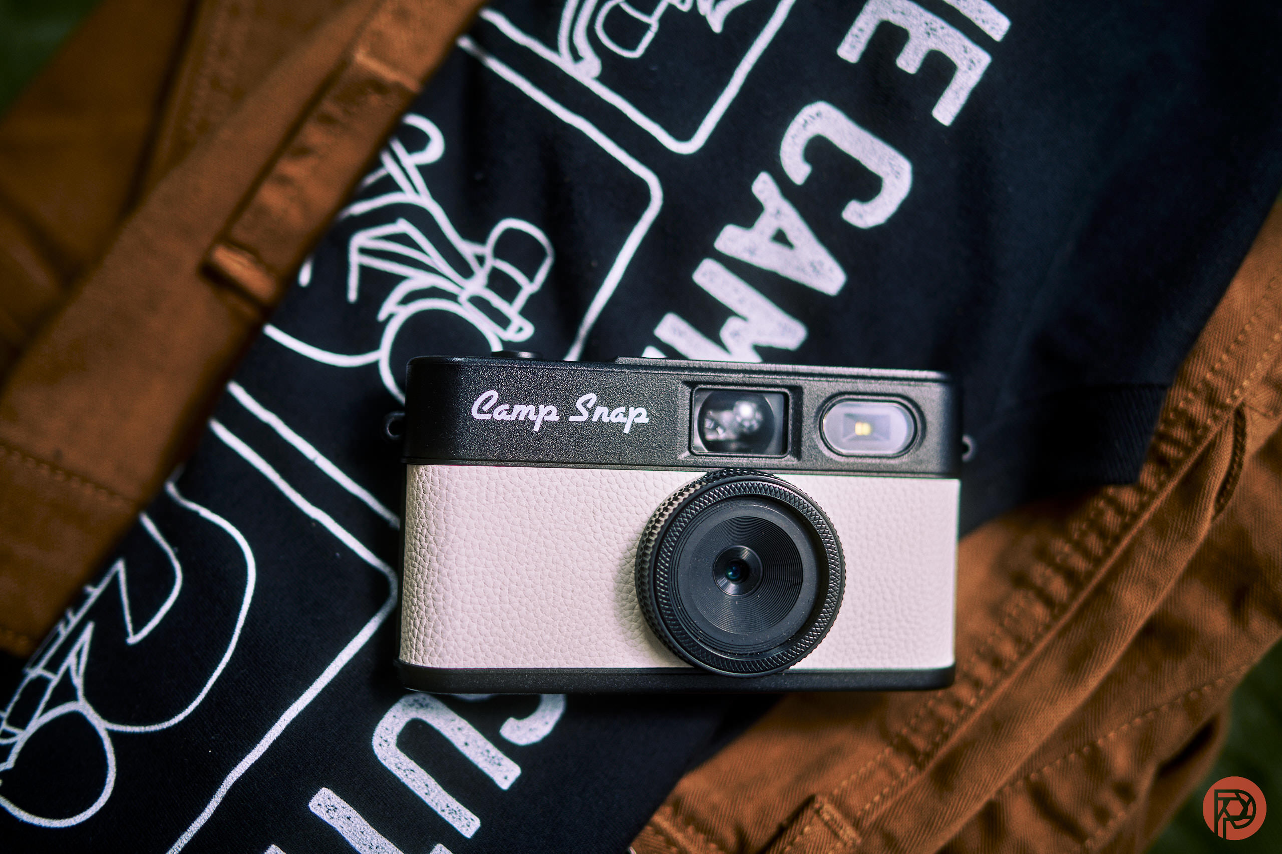 A Camp Snap camera rests on a black and white graphic t-shirt and a brown jacket.