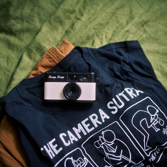 A vintage camera on a black graphic T-shirt, both laid out on a green fabric background.