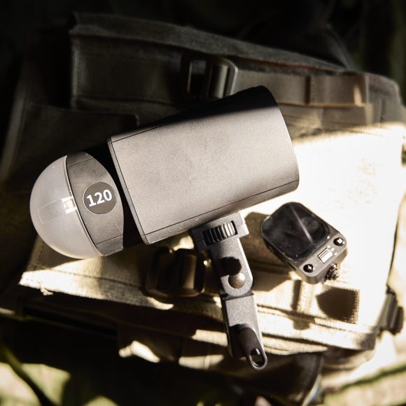 A camera flash labeled 120 and a small device rest on a beige fabric bag in sunlight.
