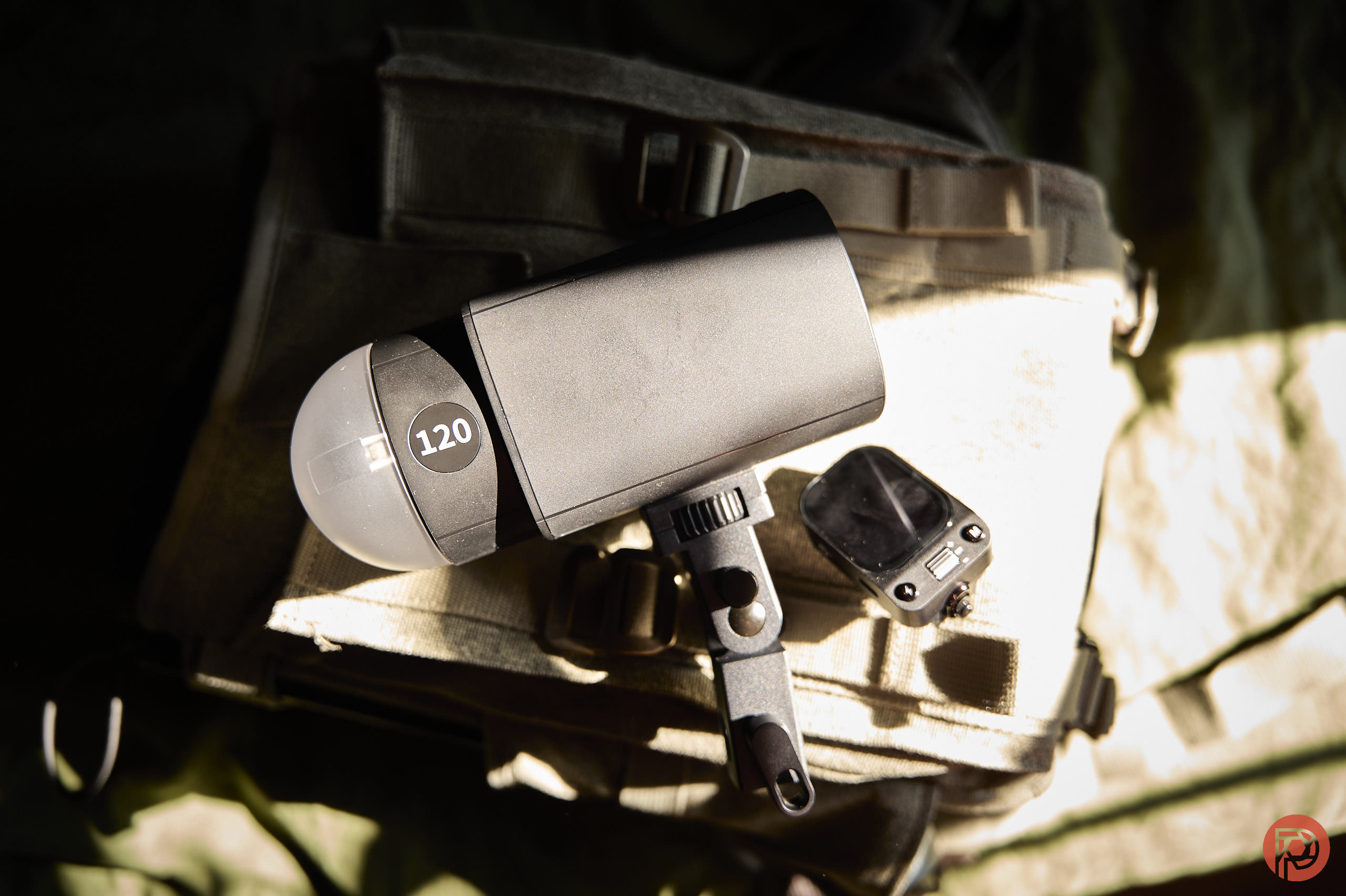Neewer Q120 Flash Review: A Great Flash for Aspiring Photographers A camera flash labeled 120 and a small device rest on a beige fabric bag in sunlight.