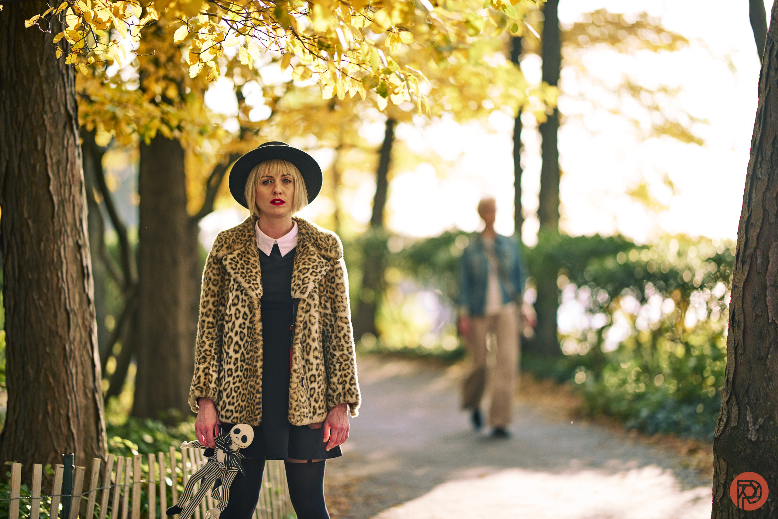 Our Analog Presets Look Incredible. Have a Look! A woman in a leopard print coat stands on a park path with autumn leaves; a person walks behind her.