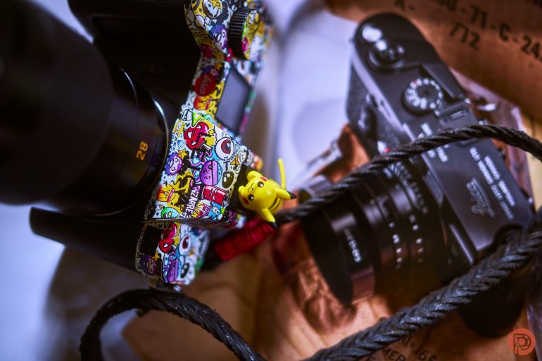 Close-up of a camera with colorful stickers and a small Pikachu figure, next to a photo of another camera.