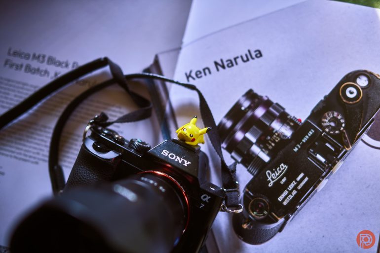 A Sony camera with a Pikachu figure sits on open pages showing a Leica camera and photography article.