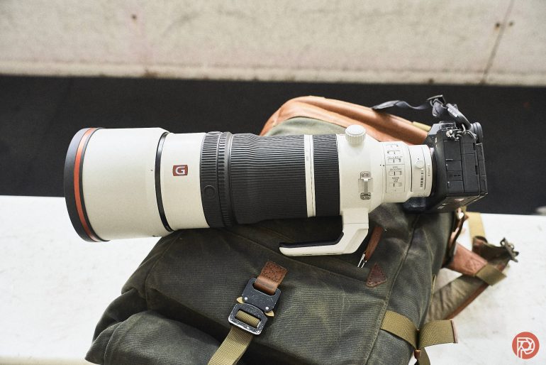 A large Sony camera with a telephoto lens rests on a green backpack.