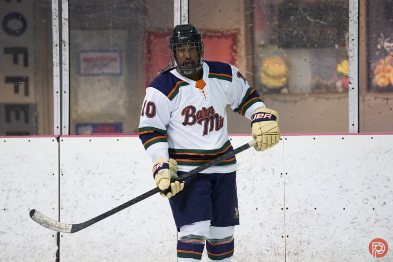 Hockey player in a Barn Mint jersey stands on the ice rink holding a hockey stick.
