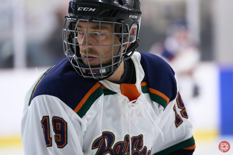 Ice hockey player in a white jersey with number 19, wearing a helmet, looking to the side on the rink.