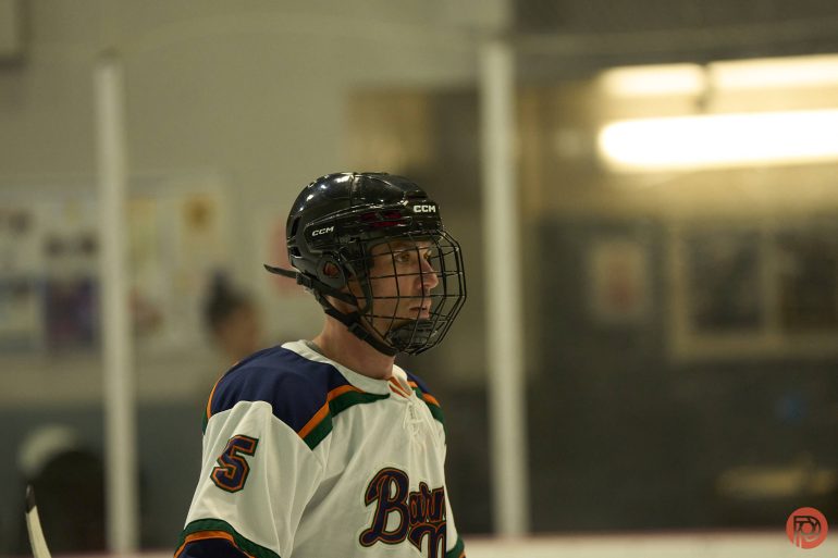 Hockey player in a helmet and jersey number 5 stands on the ice during a game.
