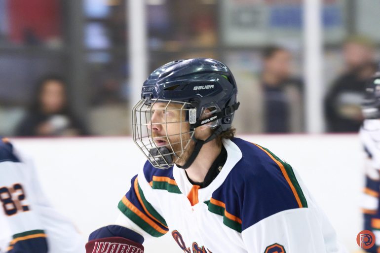Hockey player in a white and blue uniform wearing a helmet and face guard on the ice during a game.