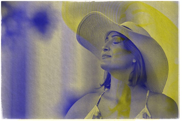 Woman wearing a sun hat with eyes closed, overlaid with blue and yellow artistic filters.