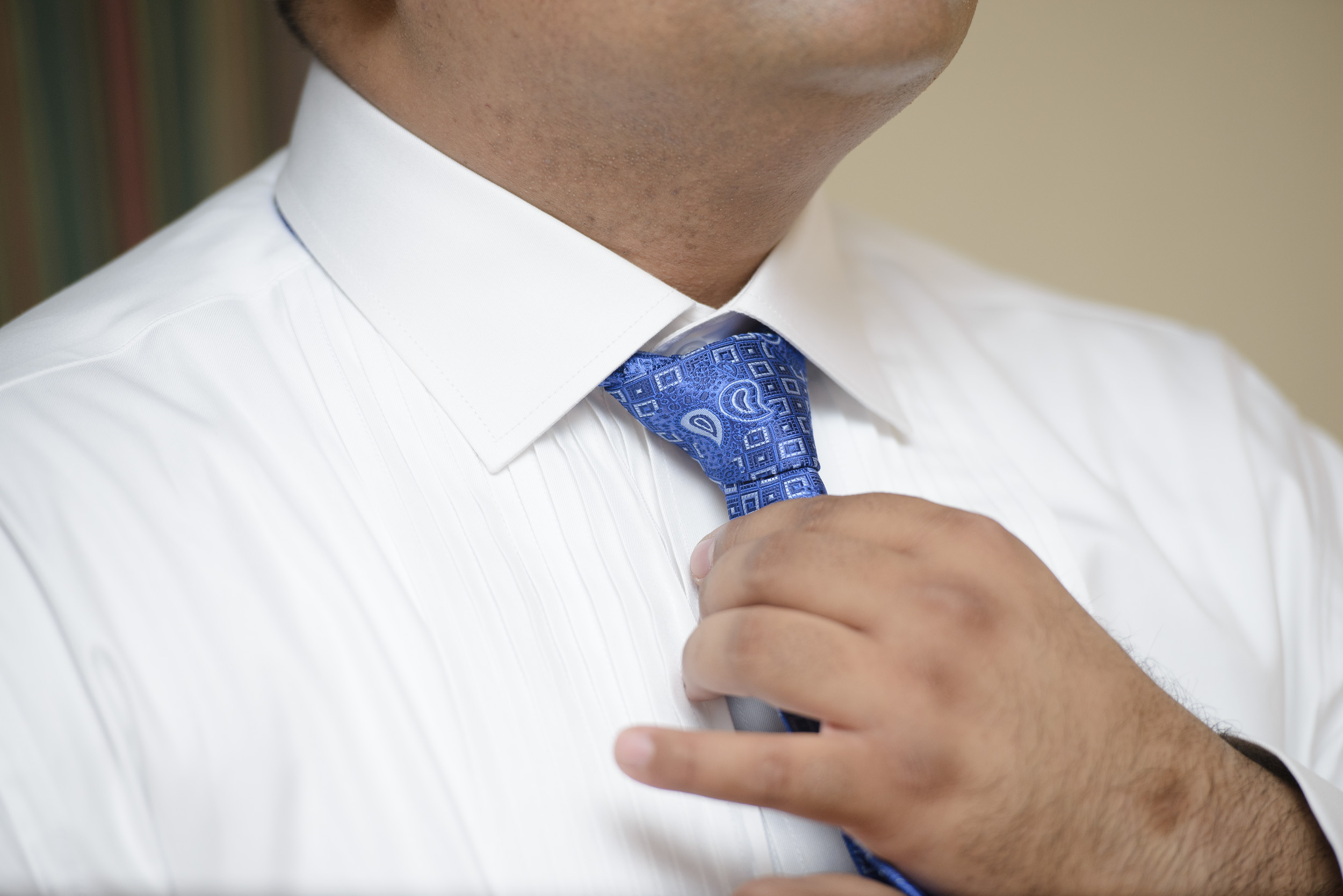 A person in a white shirt adjusts a blue patterned tie around their neck.