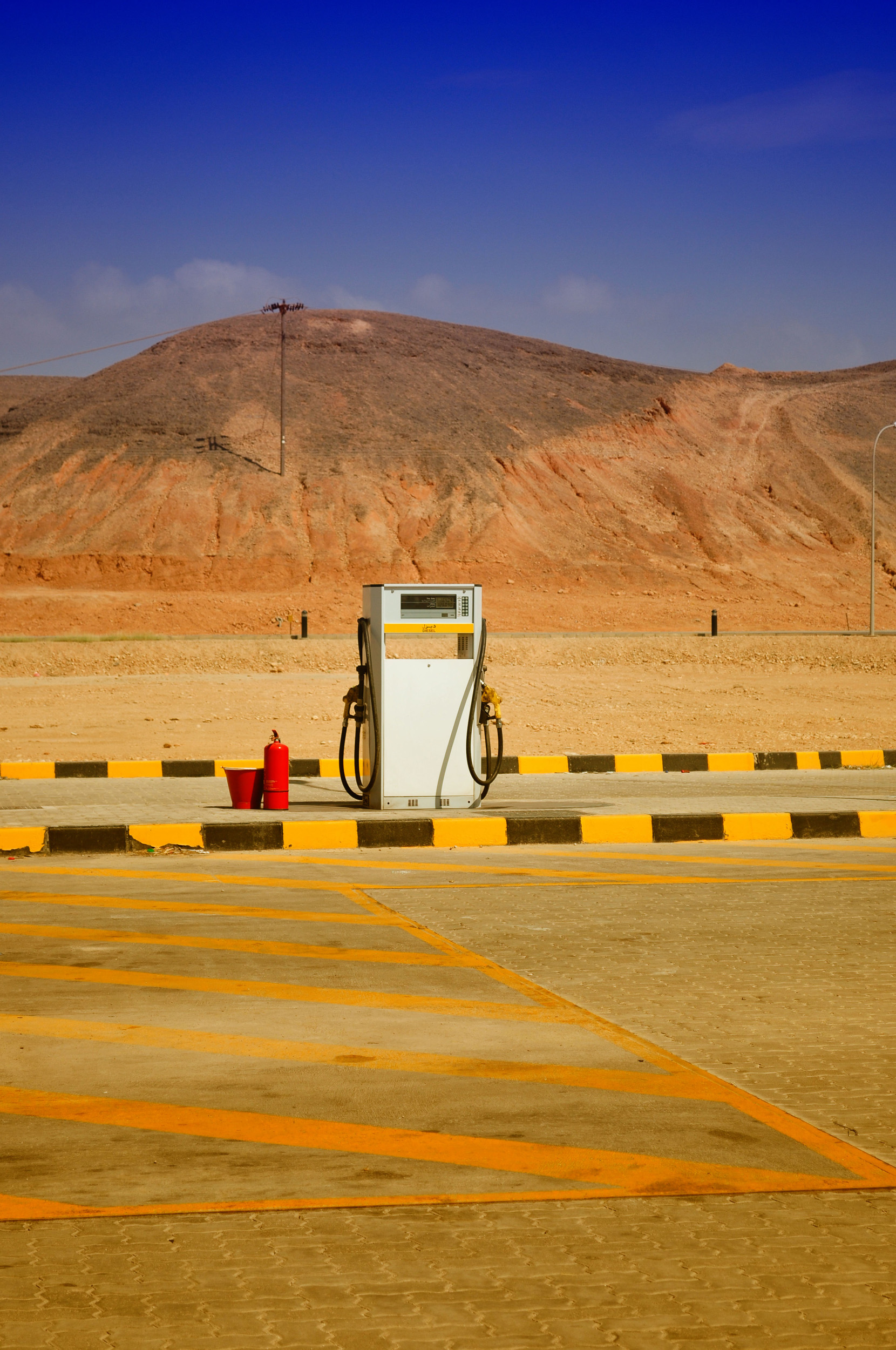 A single gas pump stands in a deserted, arid landscape with hills in the background.