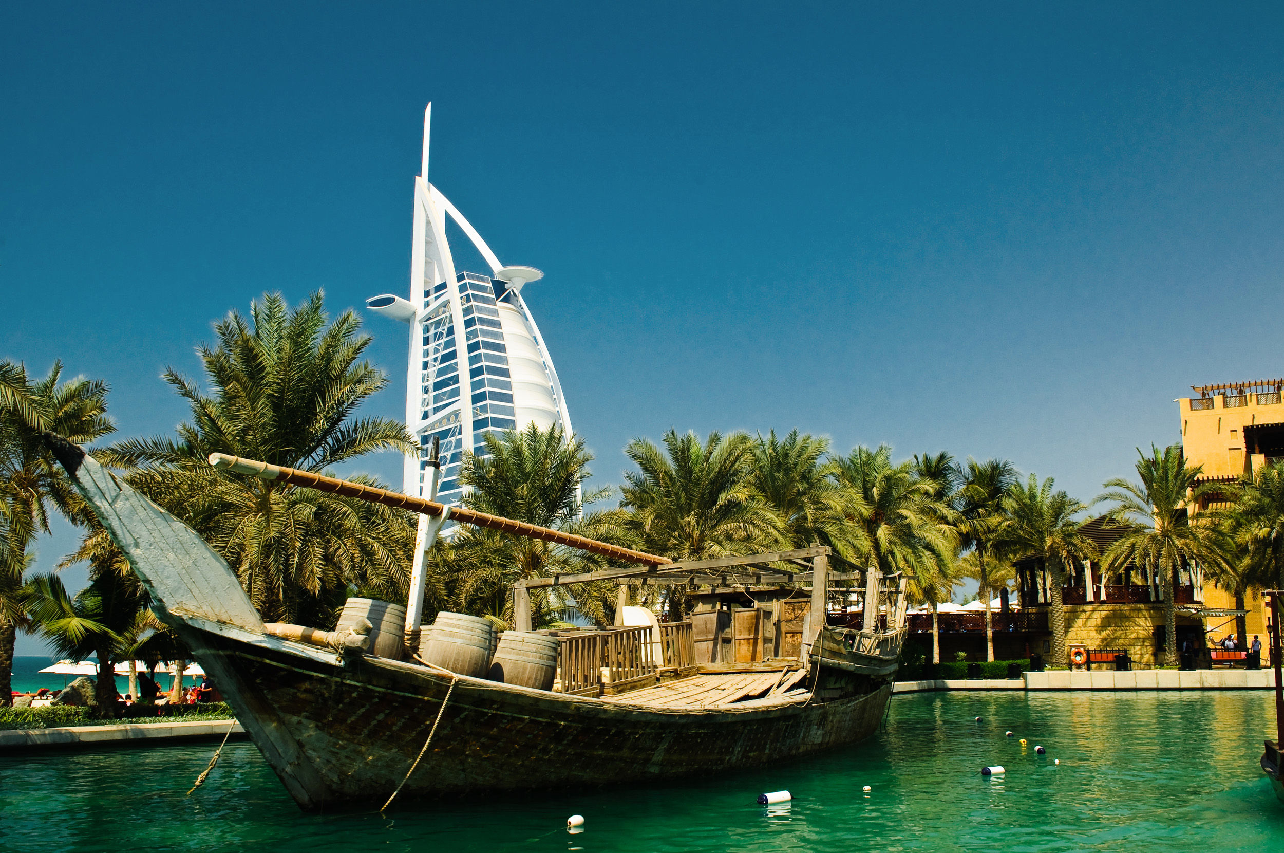 Traditional wooden boat on turquoise water with palm trees and the Burj Al Arab hotel in the background, Dubai.