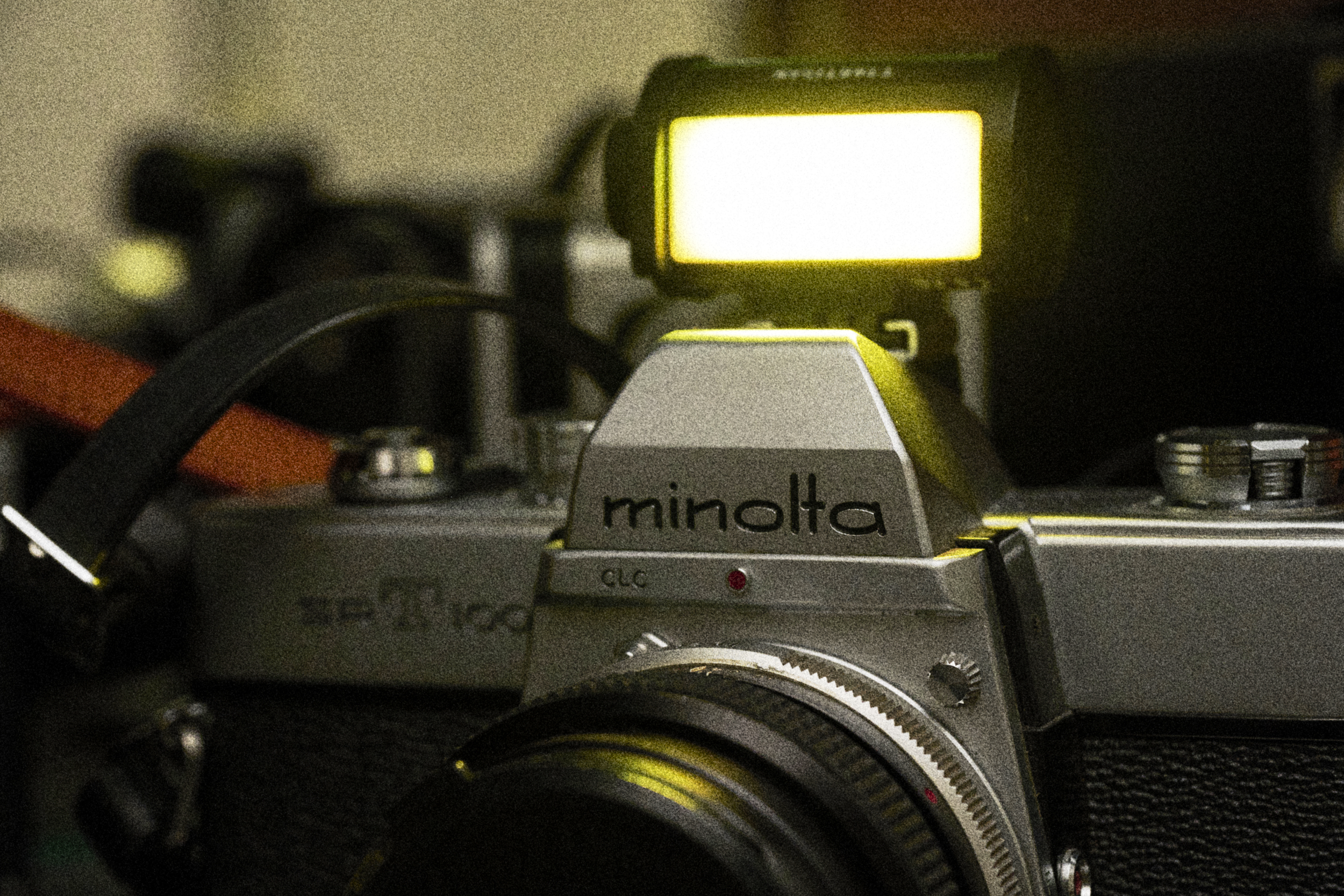 Close-up of a vintage Minolta camera with a bright flash attached and illuminated.