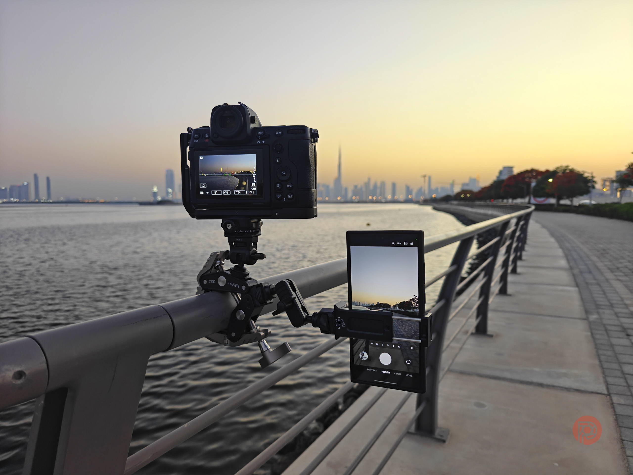 Is This the Best Replacement for a Tripod? A camera mounted on a railing captures a city skyline at sunset by the water.