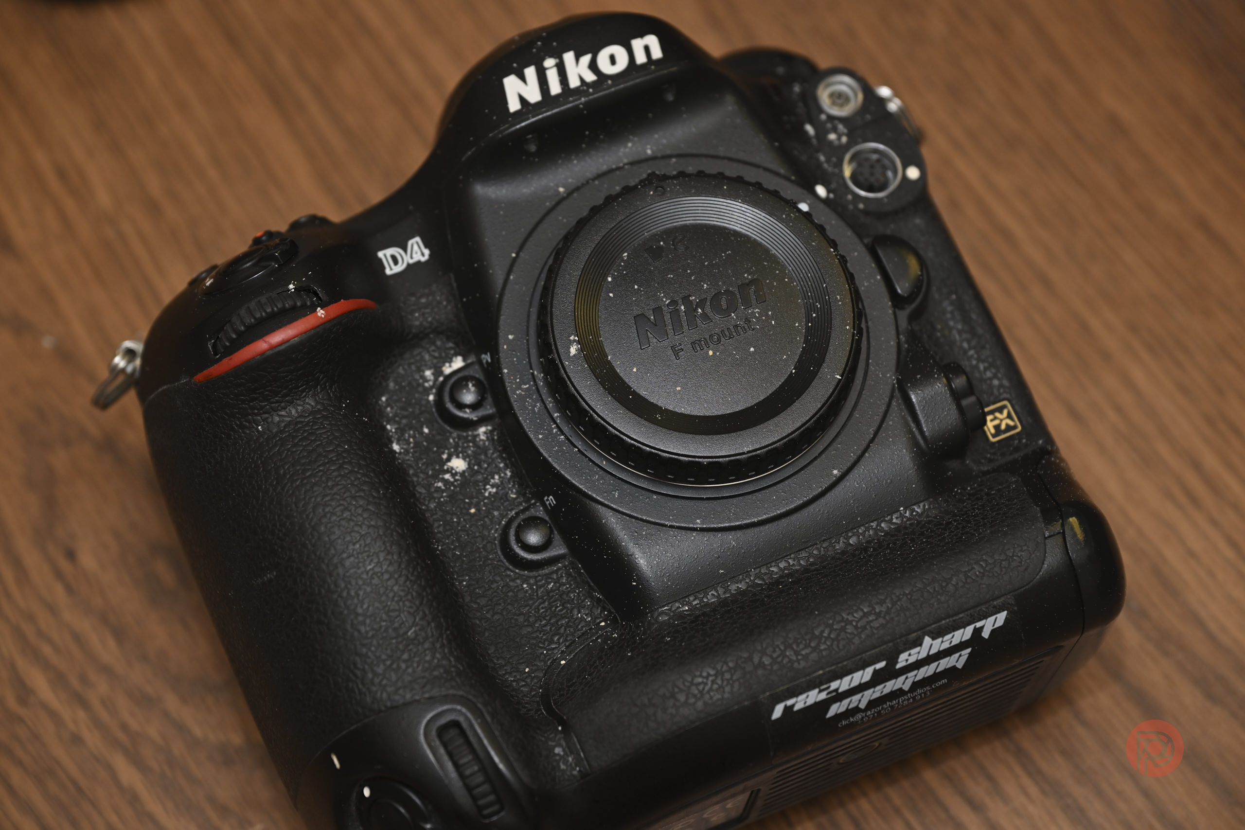 A dusty Nikon D4 camera body with a lens cap, resting on a wooden surface.