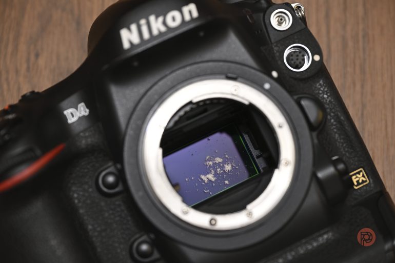 Close-up of a Nikon D4 camera with visible dust and debris on the sensor inside the lens mount.