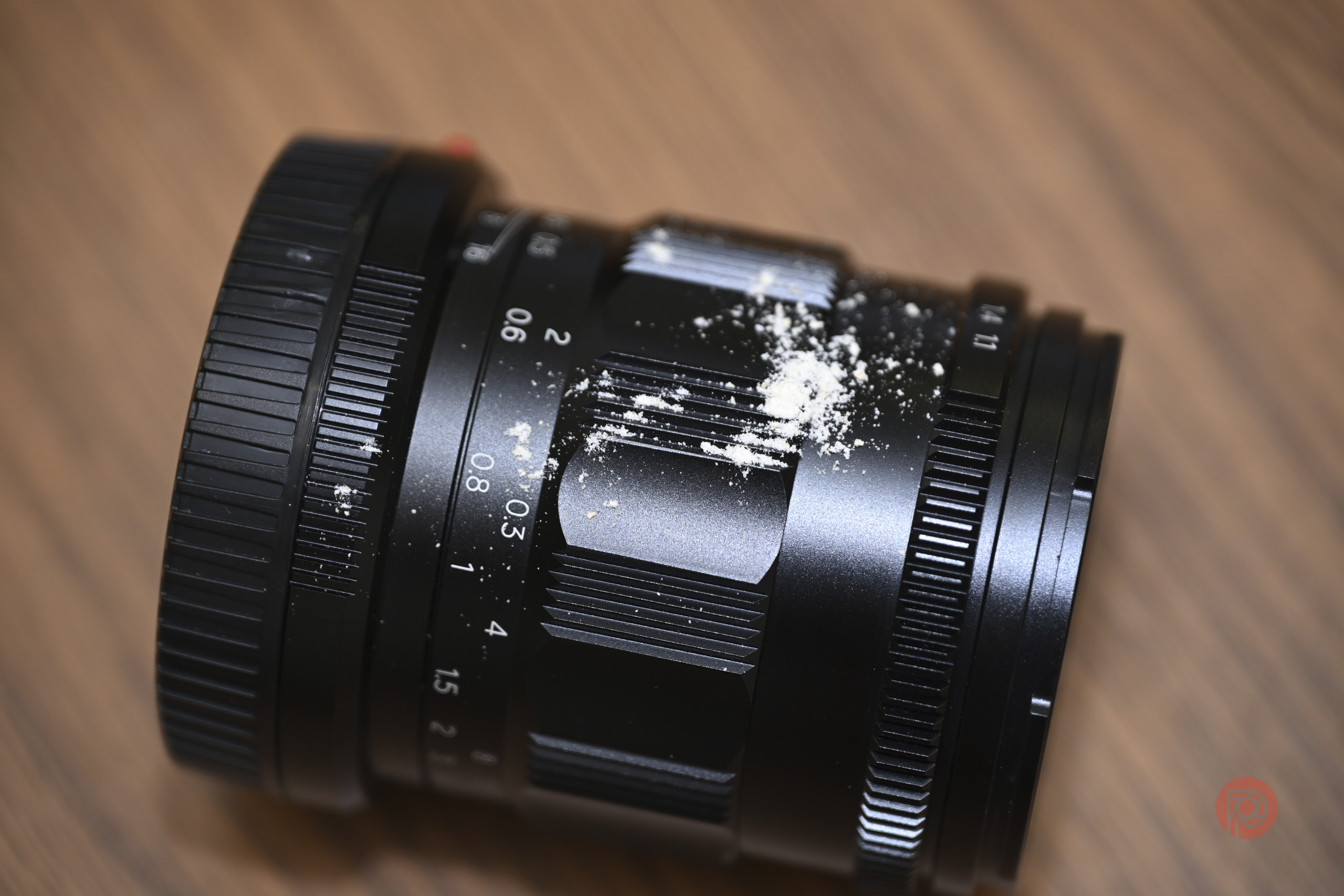 A camera lens with white powder scattered on its surface, placed on a wooden table.