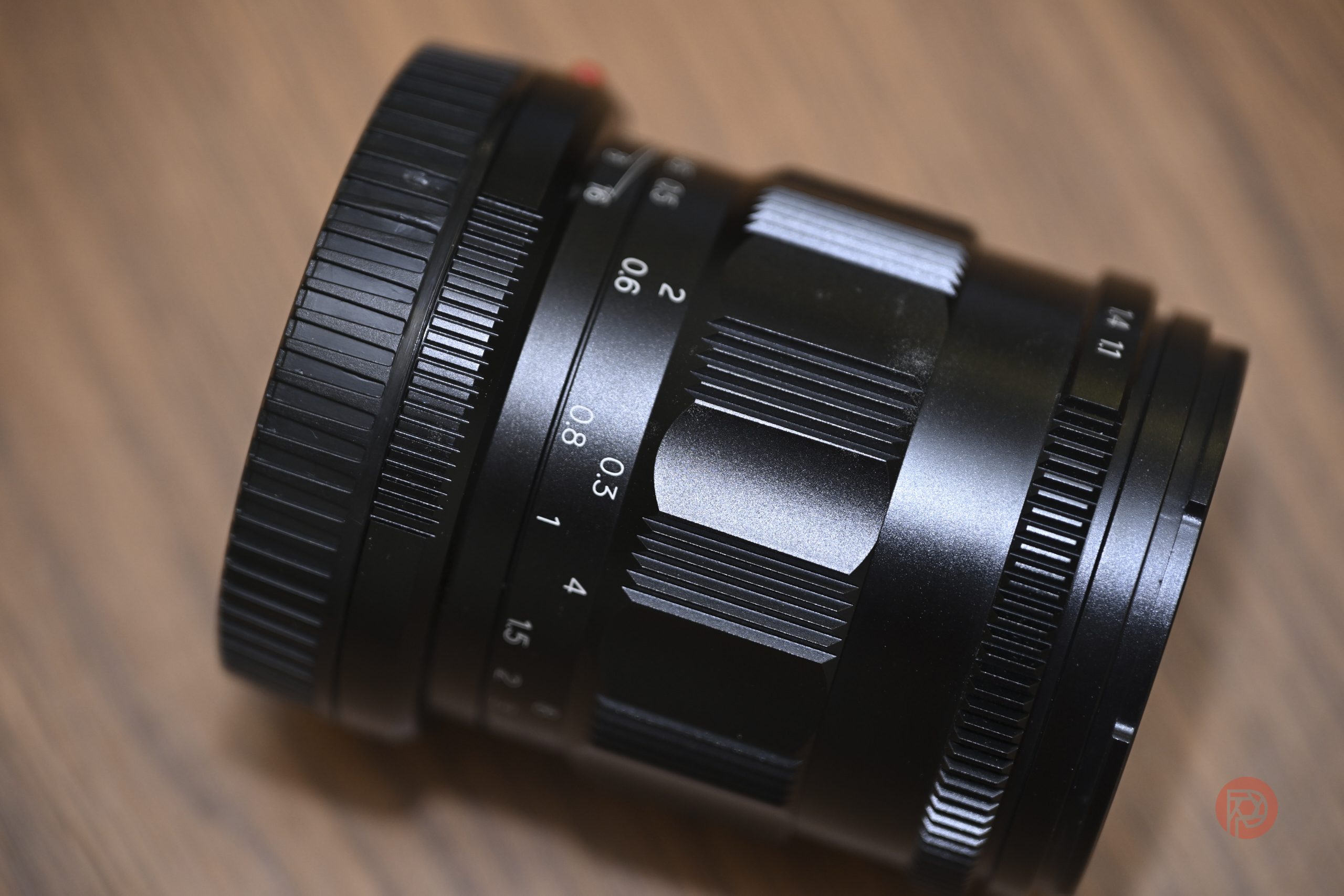 A black camera lens rests on a wooden surface, showing focus and aperture markings.