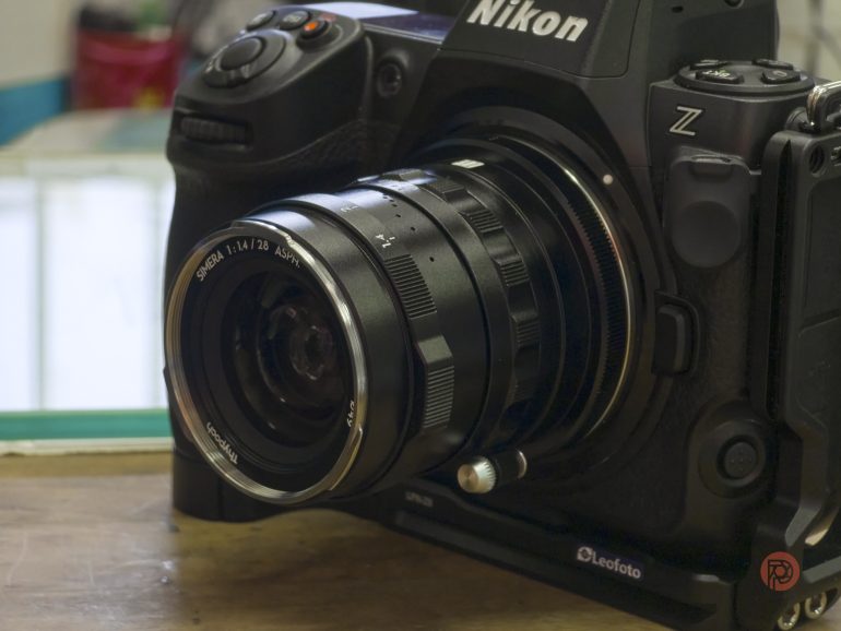 Close-up of a Nikon Z camera with a Voigtländer 28mm f/1.4 lens attached, resting on a wooden surface.