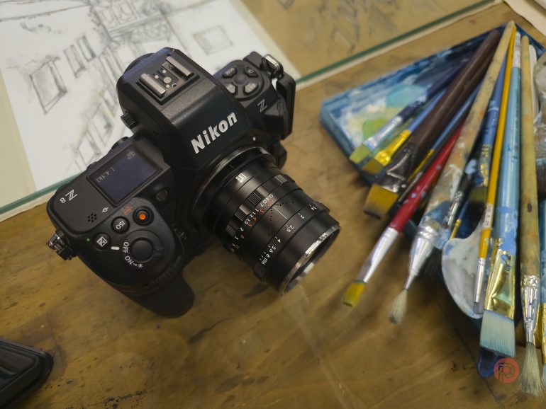 A Nikon Z camera sits on a table next to paintbrushes and sketch papers.