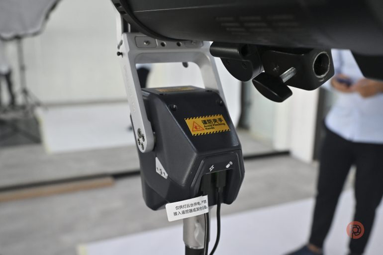 Close-up of a black motorized device with warning labels and people standing in the background.