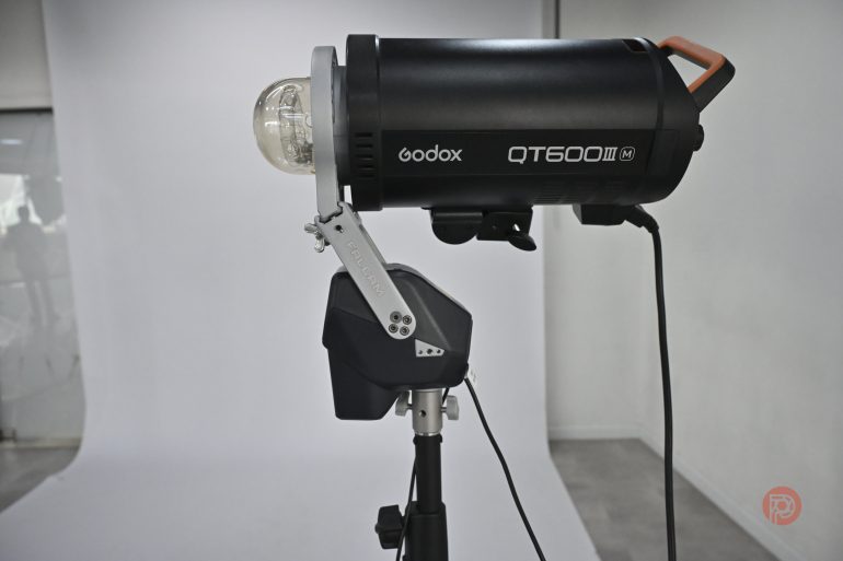 A Godox QT600II studio strobe light mounted on a stand in front of a white backdrop.