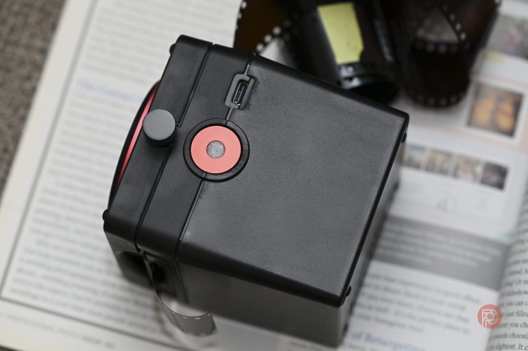 A black film scanner sits on an open magazine, with film negatives next to it.