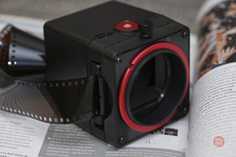 A black and red film scanner with a strip of 35mm film beside an open magazine.