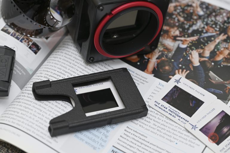 A camera lens mount and a plastic frame rest on an open magazine featuring photography articles and images.
