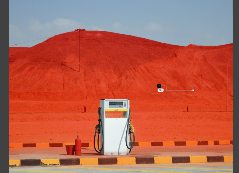 A lone gas pump stands before a strikingly bright red hill under a clear blue sky.
