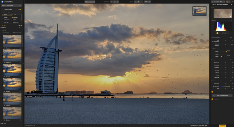 Burj Al Arab by the beach at sunset, with clouds, sunrays, and people on the sand.