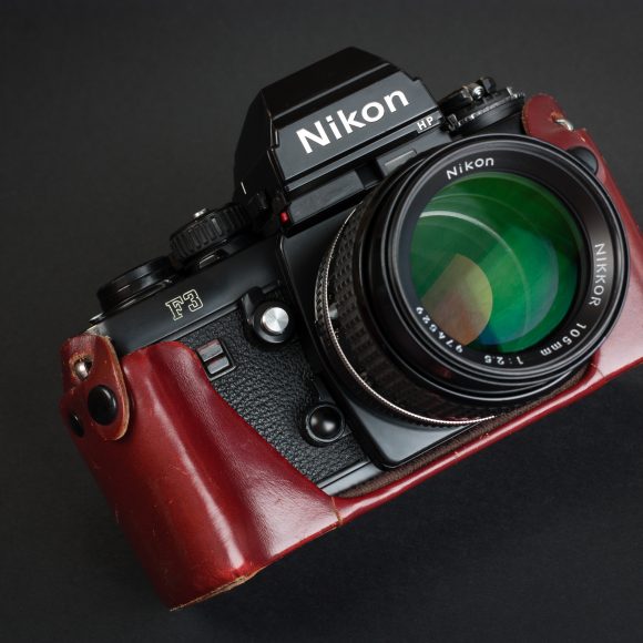 A Nikon F3 film camera with a large lens and a brown leather case on a black background.