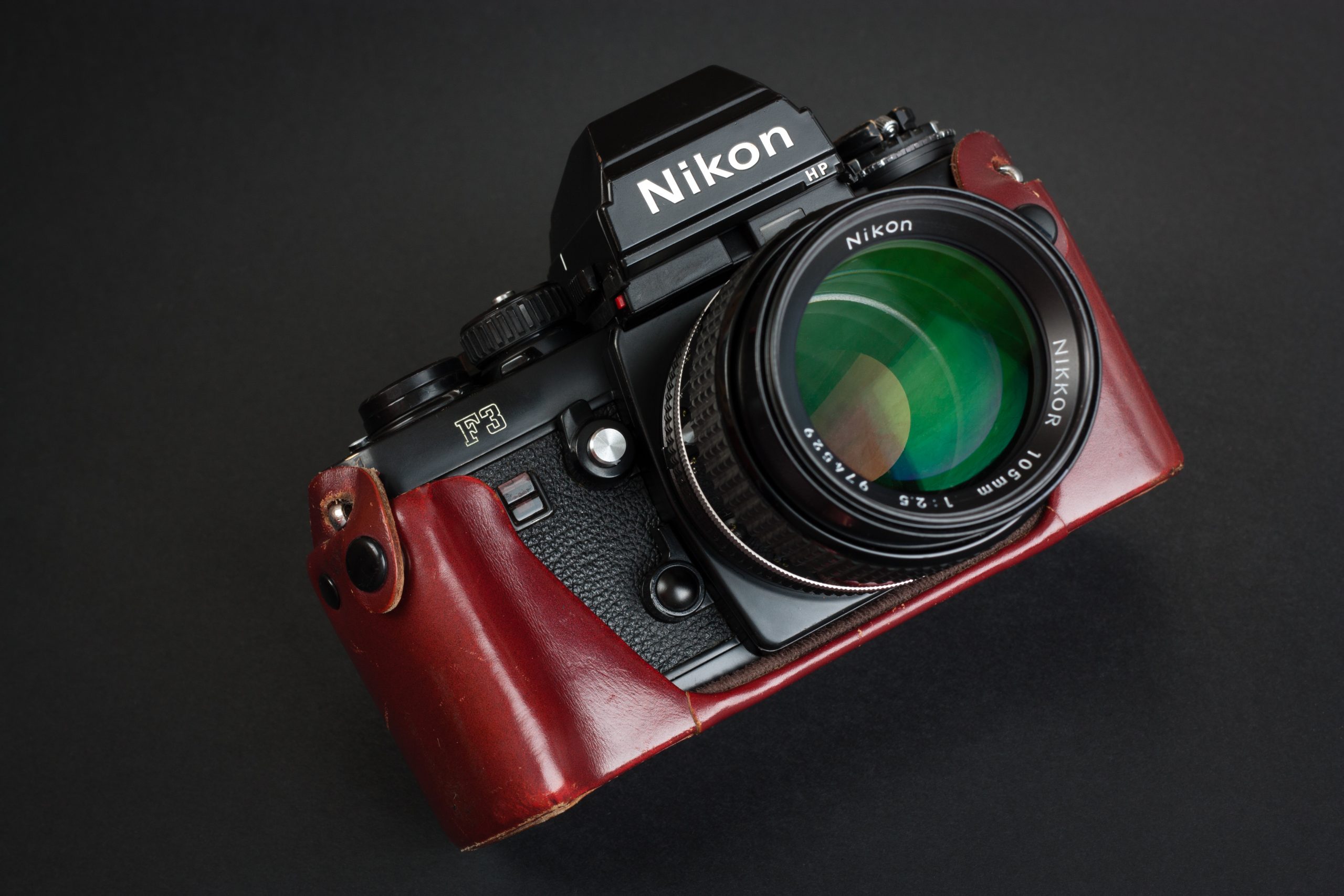 How Nikon F3 and F4 Cameras Just Got a New Lease on Life A Nikon F3 film camera with a large lens and a brown leather case on a black background.