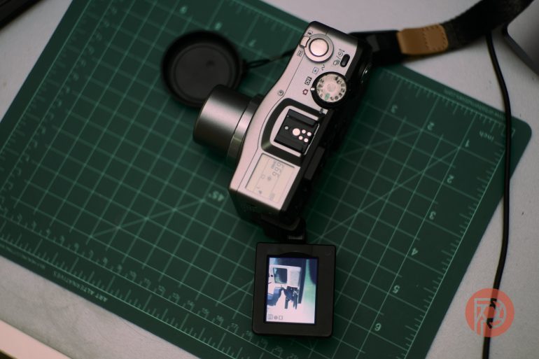 Digital camera with flipped screen on a green cutting mat, showing a photo preview on its display.