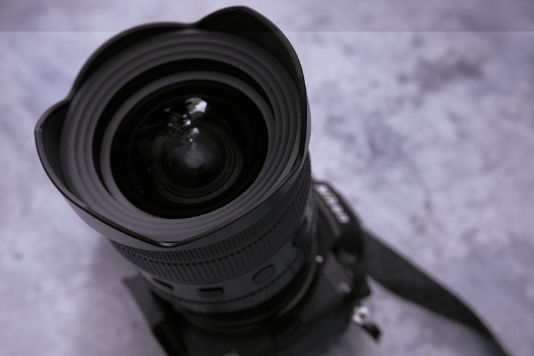 Close-up of a camera lens facing upward on a marble surface, with part of the camera body visible.