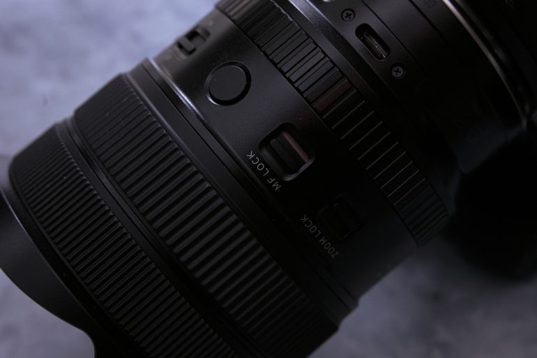Close-up of a camera lens showing the LOCK switch and part of the zoom ring on a dark surface.